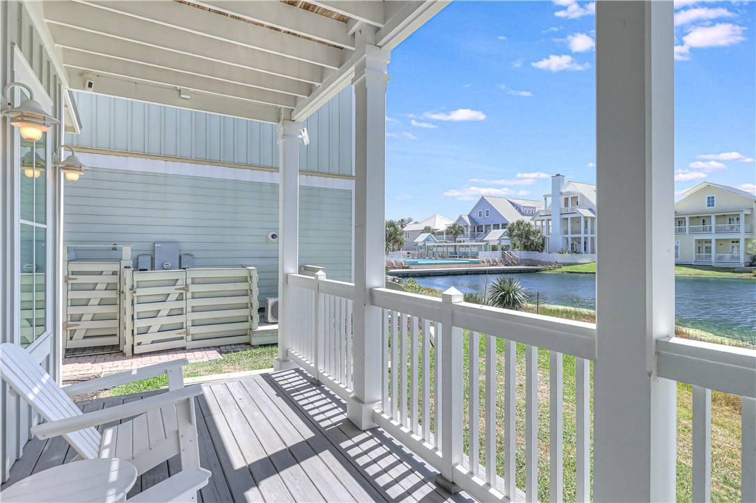 Covered porch at Beached Inn with white railings and an Adirondack chair, overlooking a lagoon and community pool at Cinnamon Shore